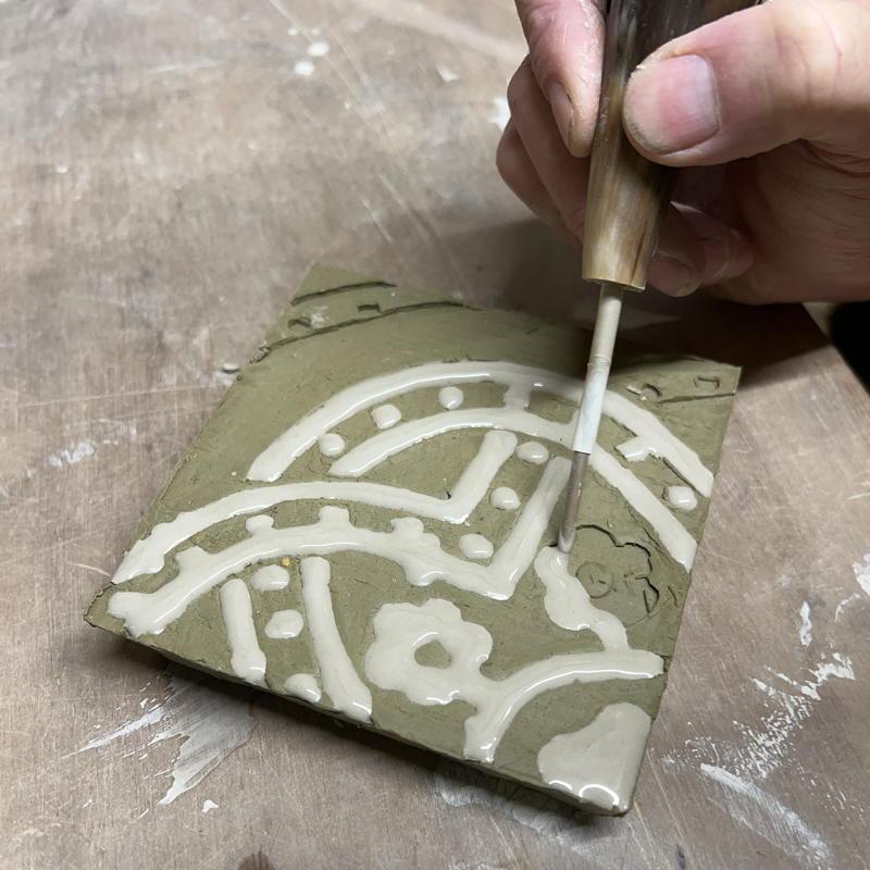 Applying white clay slip to a tile pattern